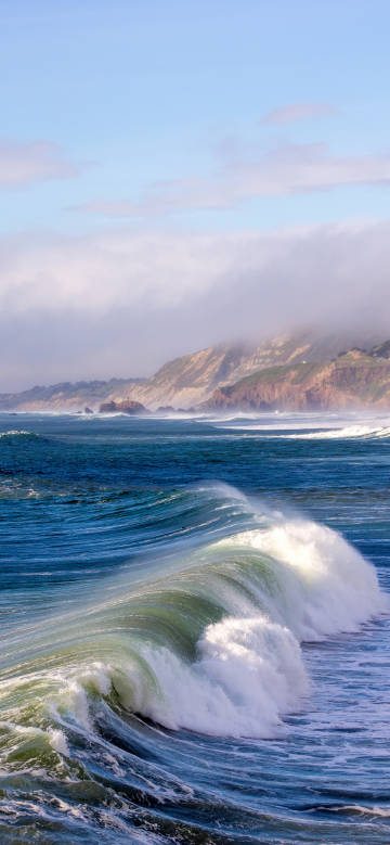 Raging waves under blue skies and white clouds